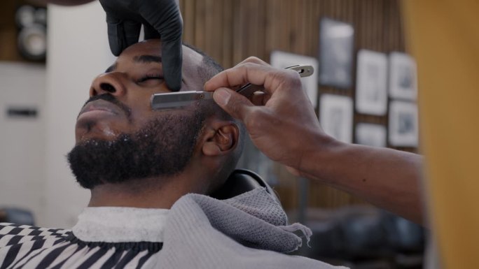 理发师在理发店用钢刀给一名非裔美国男子刮胡子