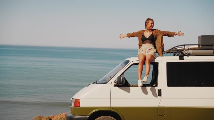 一名女子坐在停在沙滩上的房车车顶上享受着海风