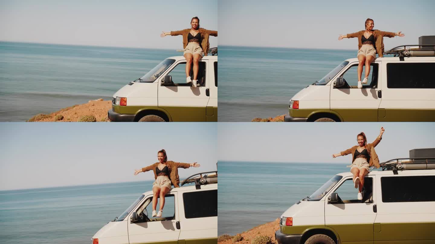 一名女子坐在停在沙滩上的房车车顶上享受着海风