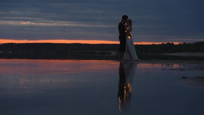 浪漫的新婚夫妇在日落后的天空中拥抱亲吻，海滩上情侣的剪影