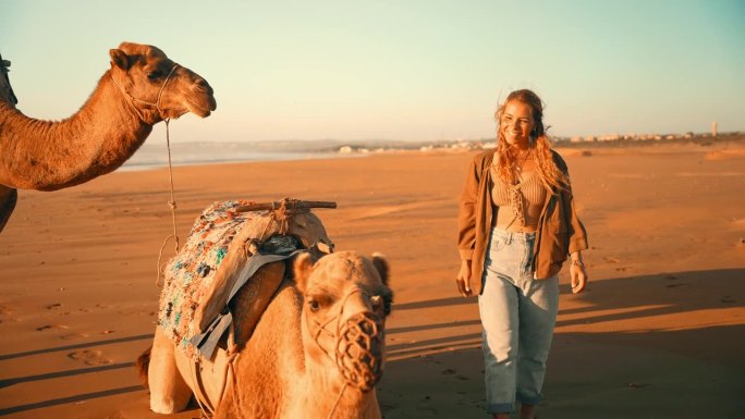 在撒哈拉沙漠的沙滩上，女游客抚摸骆驼