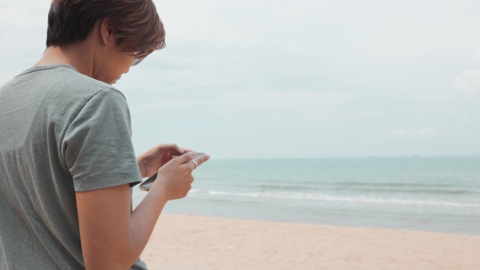 亚洲妇女在她的自由之旅和户外享受在海滩和大海。她手里拿着智能手机，捕捉快乐的瞬间，并在数字社交网络上