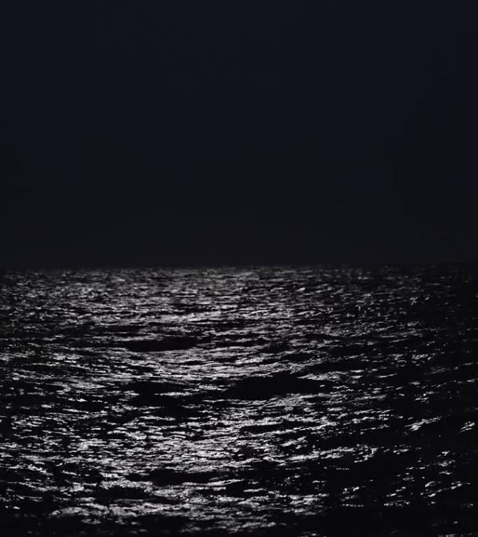 夜和月光上的海，波浪。一个年轻女子沿着海岸走的剪影，垂直，社交媒体
