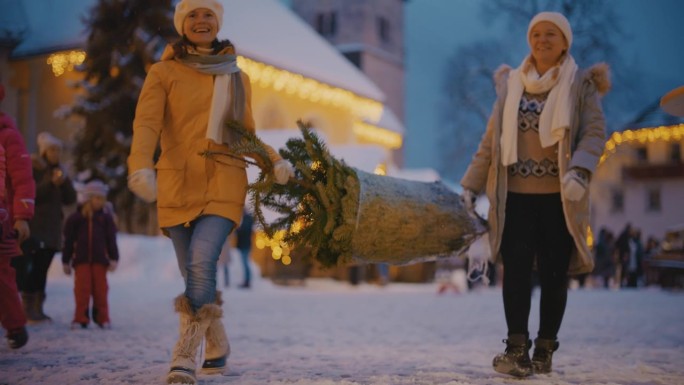 两名妇女扛着一棵圣诞树走过圣诞市场