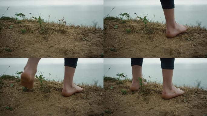 站在山顶的女人的脚特写。不知名的赤脚女孩停在干草地上。