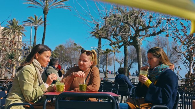 三个女人在巴塞罗那海滩的海滨酒吧喝酒。朋友们开心的聊天喝酒。只限女生旅行