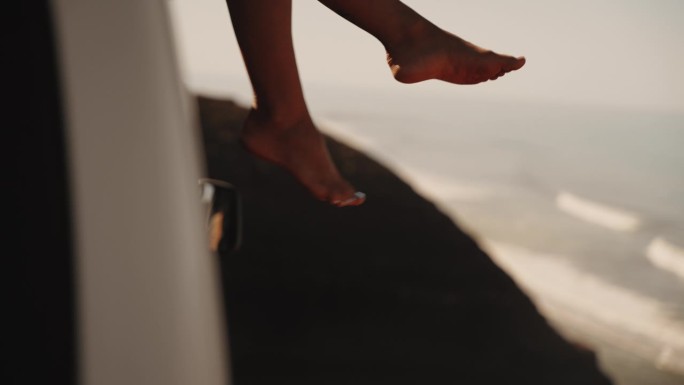 坐在露营车屋顶上享受海风的女人的双腿