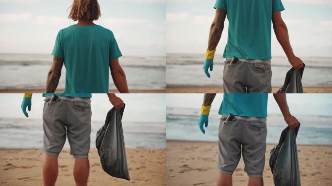 一名成年男子站在海边，拿着垃圾袋，戴着防护手套，后视图