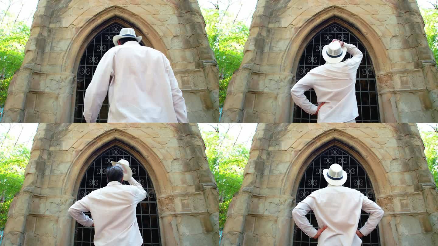 一个戴着白色草帽的男人走近一座古老的哥特式建筑的拱门。他脱下帽子，又戴上帽子。他突然转过身来，脸上露