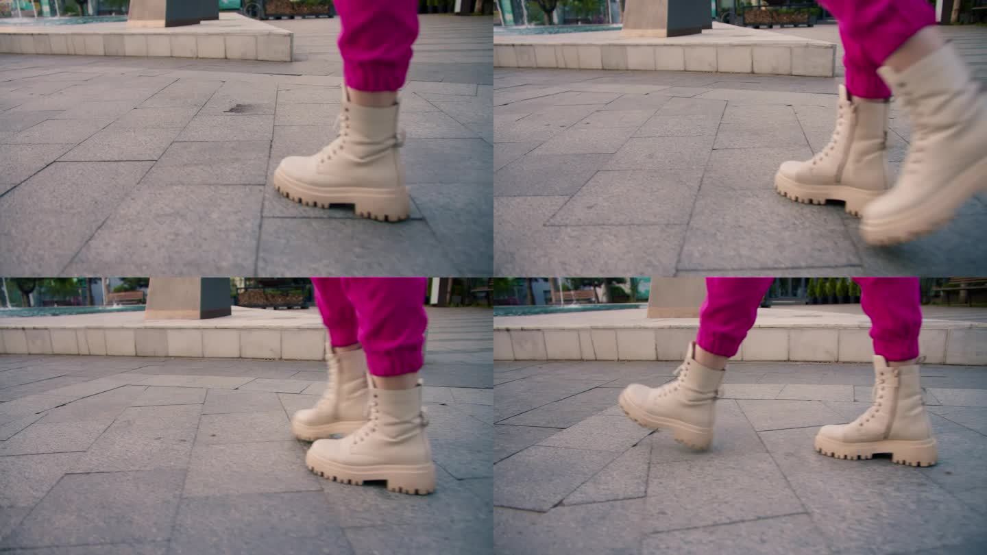 近距离拍摄，一个穿着粉色裤子和白色运动鞋的女孩走在街上。在画面中，一个女孩的行走腿，一个快乐的夏日漫