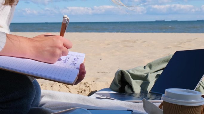 年轻的学生在海边的沙滩上拿着笔记本学习。写感恩日记自我反思自我发现自我发现，日记，自我反思，创意写作