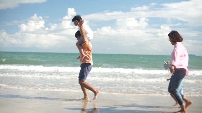 亚洲家庭带着快乐的情绪在海滩上奔跑