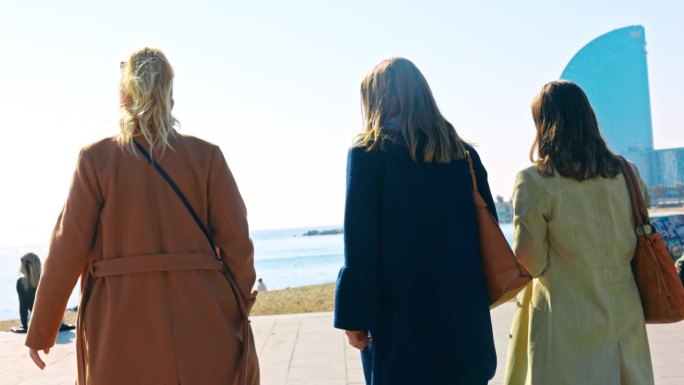 三个女人并排走在巴塞罗那海滩上