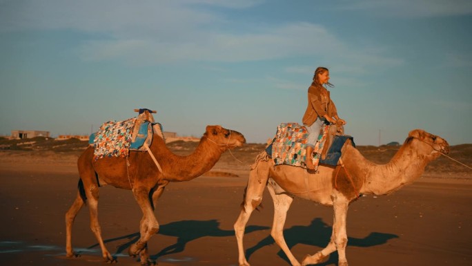 女游客在沙滩上骑骆驼玩得很开心