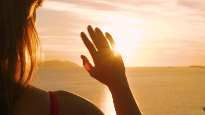 特写，镜头光晕:女性的手在亚得里亚海金色的夕阳下挥手