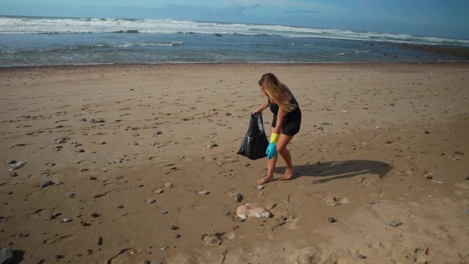 年轻女子在海边捡垃圾，把垃圾放进垃圾袋里