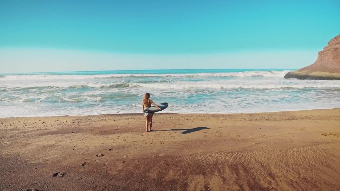 在阳光明媚的海滩上，女性拿着冲浪板寻找完美的冲浪点