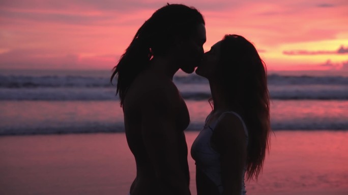一对相爱的人在海边，日落和海水。现代白人家庭的两个恋人放松地看着对方并亲吻。漂亮女人和有吸引力的英俊