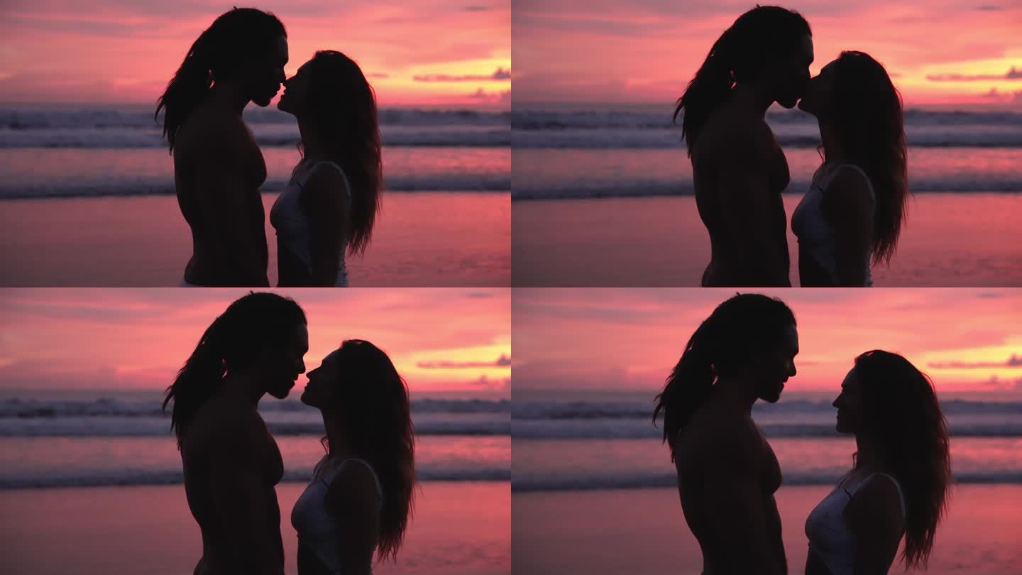 一对相爱的人在海边，日落和海水。现代白人家庭的两个恋人放松地看着对方并亲吻。漂亮女人和有吸引力的英俊