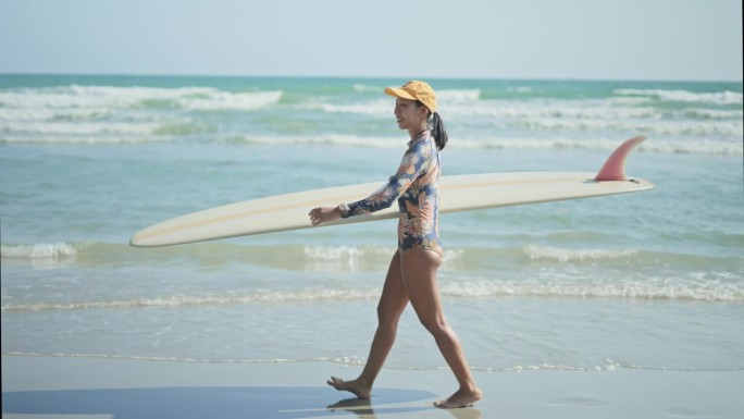 女冲浪者带着冲浪板在沙滩上行走，慢动作