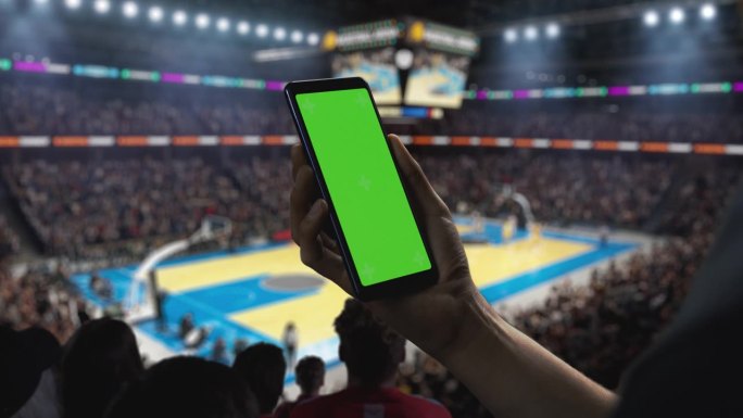 篮球锦标赛:手持绿屏智能手机的人。体育场上的球迷为球队的胜利欢呼。模板用于社交媒体，分数，结果，投注