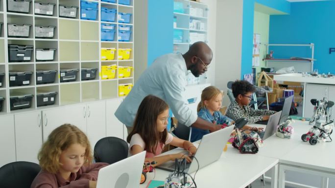 在机器人俱乐部里，黑人男老师看着孩子们在笔记本电脑上学习