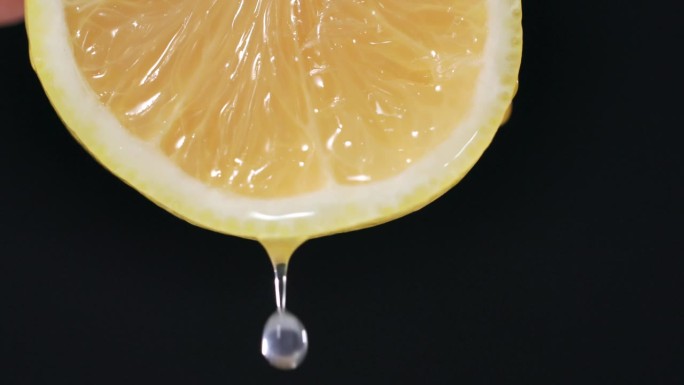 美味多汁的柠檬，一滴水或果汁流下一片柠檬在黑暗的背景，特写