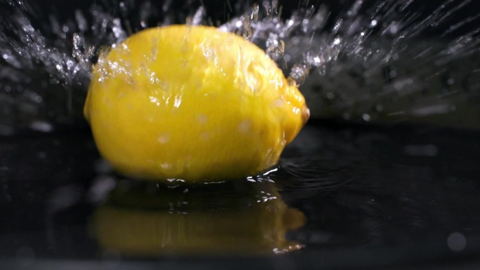 熟透的新鲜柠檬落入一盘水中，背景为深色，特写