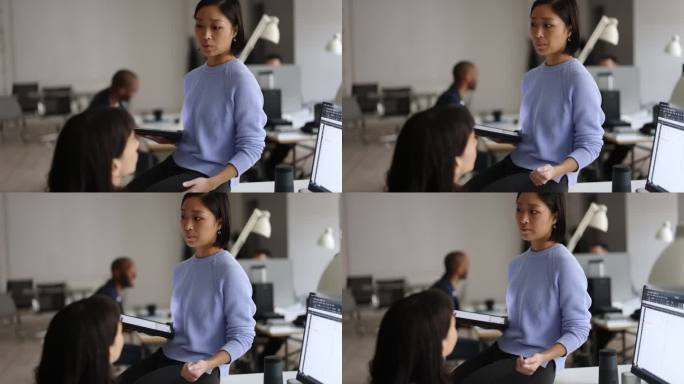 在联合办公办公室里，一名年轻的亚洲女性正在和她的女同事交谈