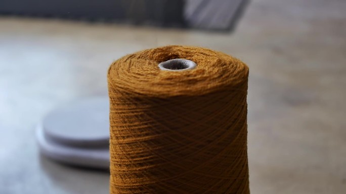 一根橙色的羊毛线从地板上的一根大麻纱上解开。羊毛及纺织工业