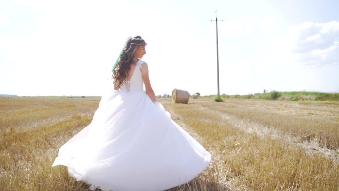 快乐的年轻女子穿着白色的裙子在麦田里奔跑。慢动作