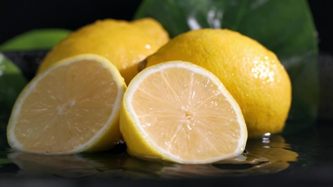 柑橘类水果，成熟的柠檬躺在水里，黑暗的背景，一片柠檬落在果肉上，水珠散落在不同的方向，特写