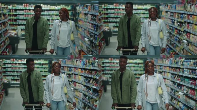 一对黑人夫妇走在超市的过道上愉快地聊天。男伴侣推着车，女伴侣买东西