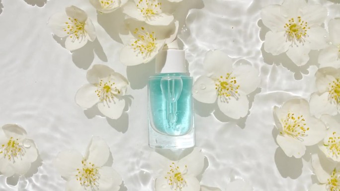 化妆品瓶、瓶和茉莉花花瓣在水面上滴着。纯净的水反射阳光和阴影。缓慢运动的海浪。设计、广告、产品
