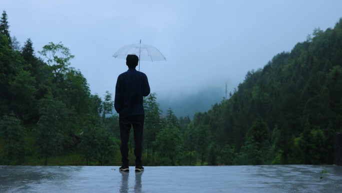 男人在雨天打着透明的伞看山