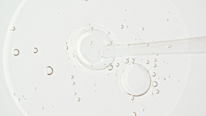 透明的化妆品凝胶液，血清与分子气泡油在移液管滴在一个白色的背景。天然有机化妆品、药品微距拍摄。生产特