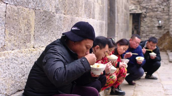 一群人蹲在墙根吃饭