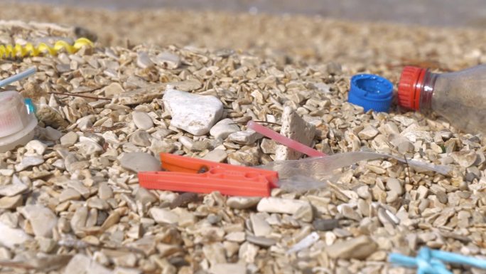 特写:被冲上岸的塑料垃圾残留在卵石海岸上，种类繁多，令人惊叹