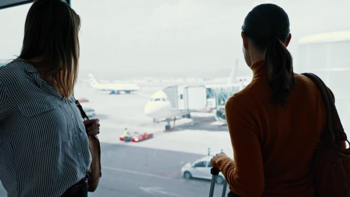 中景:两位女性朋友在机场登机口使用智能手机，等待登机