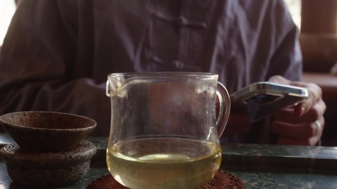 茶艺大师使用智能手机在茶道上等待整个茶水冷却。