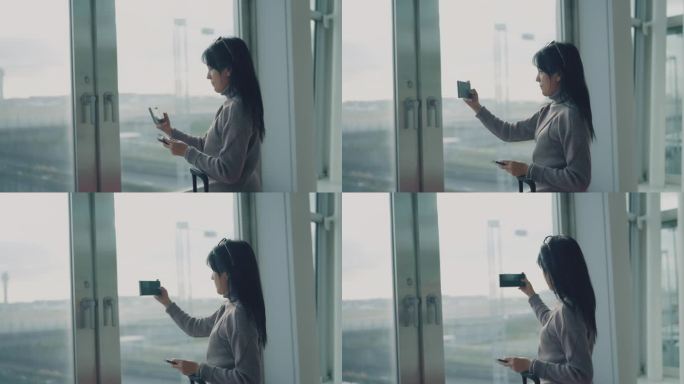 一名亚洲女子站在机场窗口，用智能手机拍照