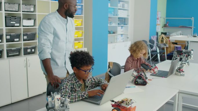 黑人男老师在机器人俱乐部用笔记本电脑照看孩子