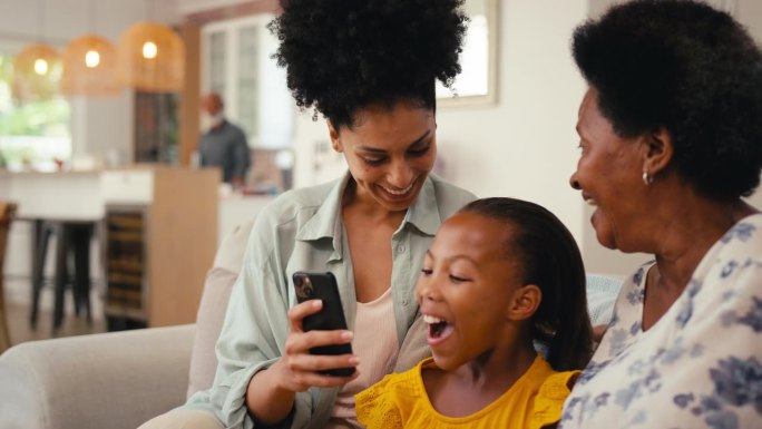 多代女性家庭一起坐在家里的沙发上用手机看社交媒体