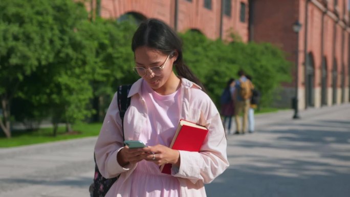 亚洲女学生背着双肩包用手机打短信走向大学的滑块镜头