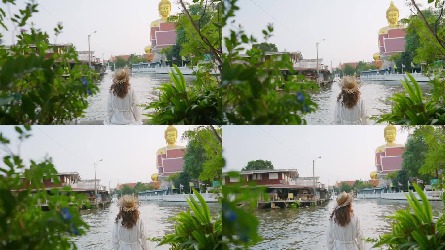一名女子坐在曼谷的河岸上，看着巨大的金佛雕像