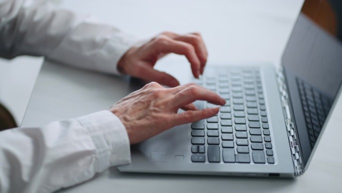 在办公室工作的老年妇女，现代笔记本电脑键盘上女性的手特写
