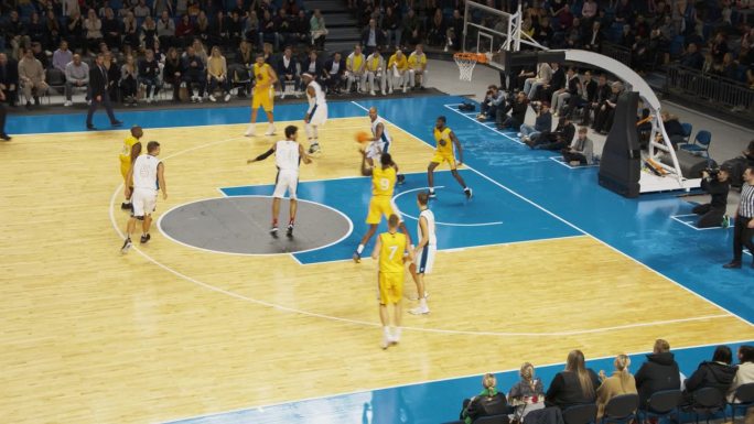 现代竞技场上的篮球比赛:黄队进攻篮筐，将球传给明星球员，明星球员成功扣篮得分。体育电视广播回放