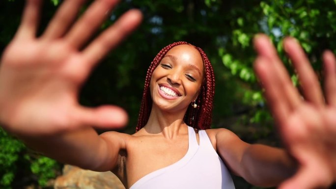 户外写真自然美丽的年轻非洲裔美国妇女红辫子发型，完美的白色牙齿微笑，笑着用手在阳光明媚的夏日与绿色的