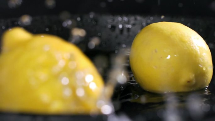 柑橘类水果，成熟的柠檬落入一盘水中，水花散落在不同的方向在一个黑暗的背景，特写