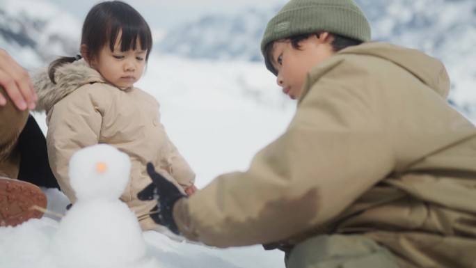 可爱的小女孩和她的家人坐在雪地上向上看。她看着弟弟堆雪人。